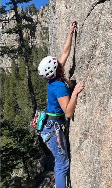 Climber performing lock off position with right arm to reach for a rock climbing hold with her left hand.