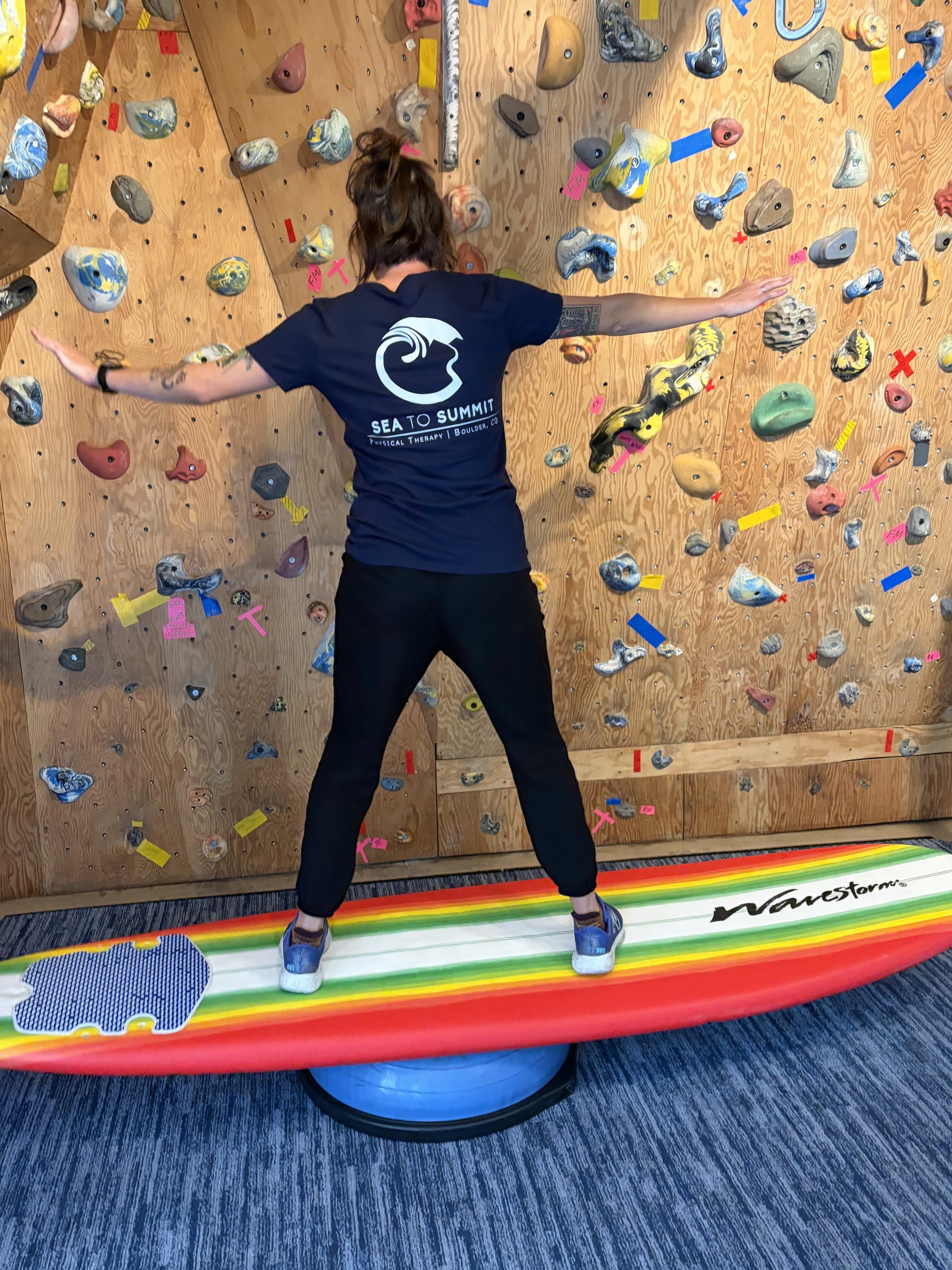 Person balancing on surfboard, back of shirt reads: Sea to Summit Physical Therapy, Boulder, CO